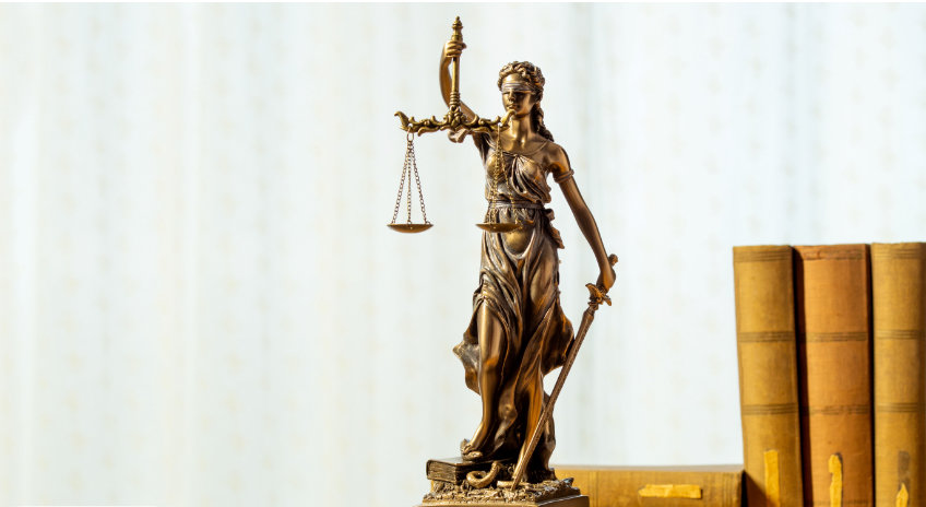 Justitia mit Waage und Schwert vor einem Bücherregal